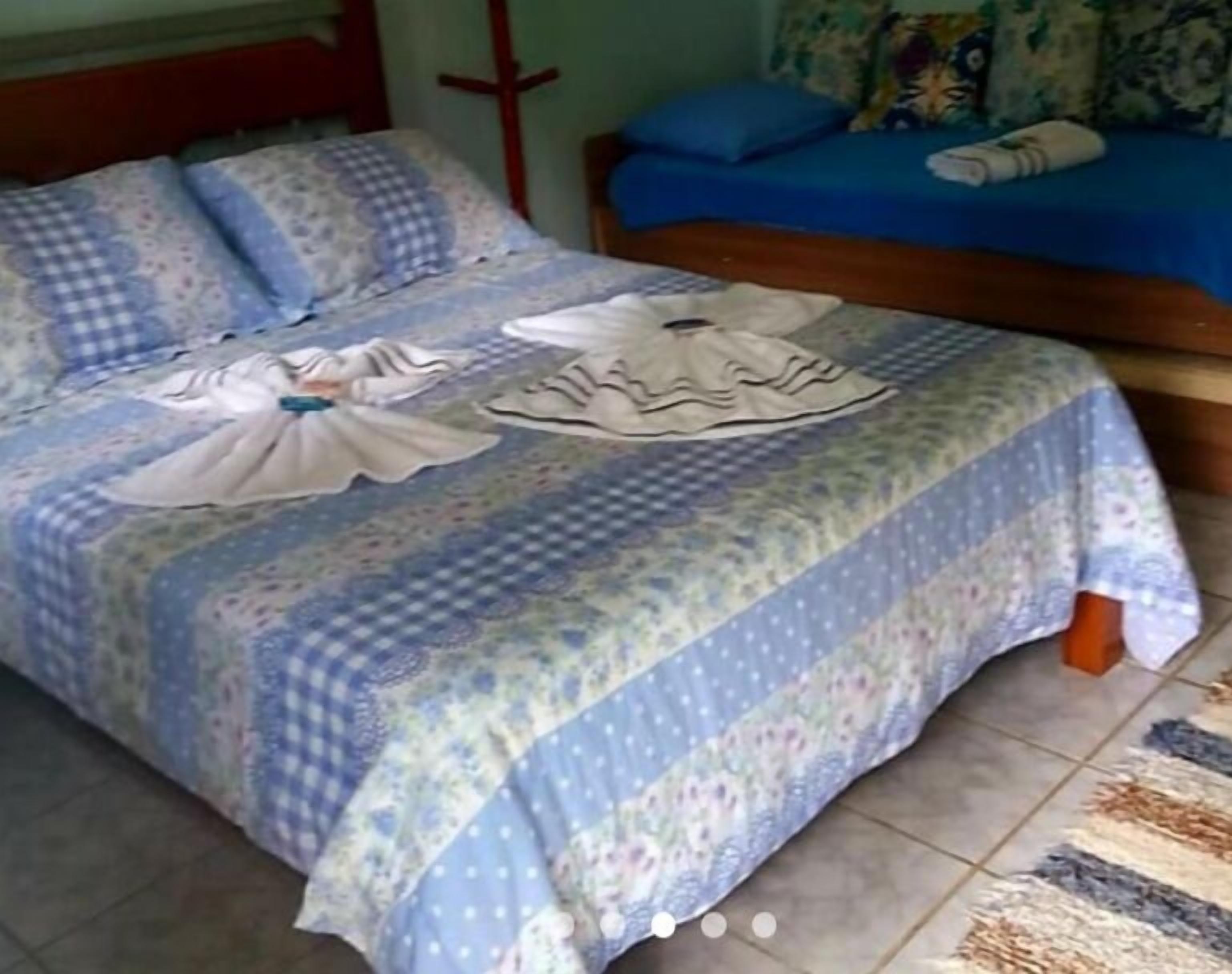 Una cama con una colcha y almohadas estampadas, un sofá azul con un cojín decorado, y una cruz en la pared.