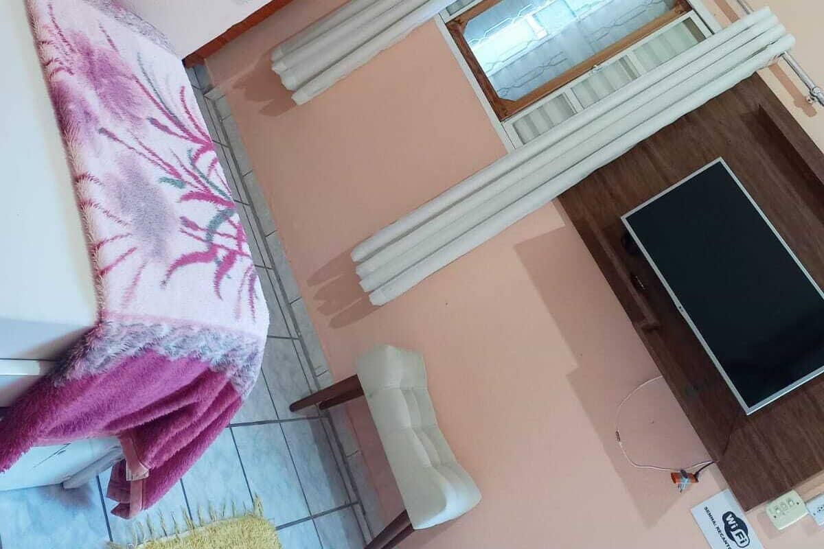 A room with a bed, a TV, a window with blinds, and a mirror.