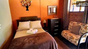 A hotel room with a bed, a dresser, a chair, a mirror, and a wall decoration. - POUSADA SERRANO (São Bento do Sapucaí)