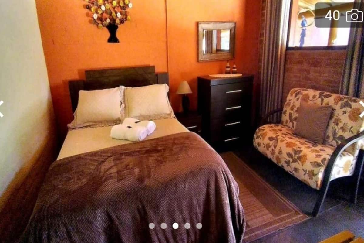 A hotel room with a bed, a dresser, a chair, a mirror, and a wall decoration.