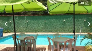 A poolside area with green umbrellas, white plastic chairs, and a tiled patio. - POUSADA SERRANO (São Bento do Sapucaí)
