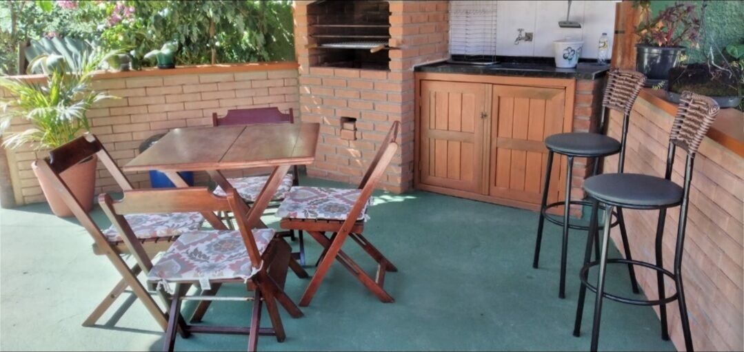 An outdoor patio with a brick barbecue, wooden table and chairs, and a small bar area.