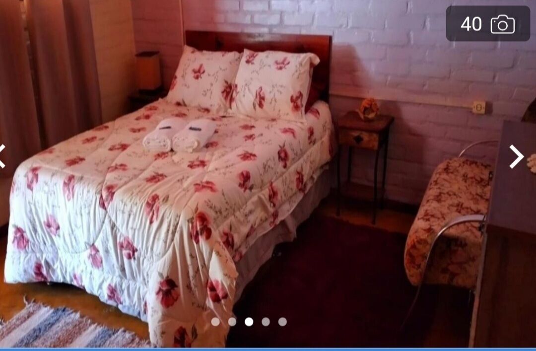 A bedroom with a floral bedspread, a wooden headboard, a nightstand, and a bedside table with a lamp.