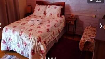 A bedroom with a floral bedspread, a wooden headboard, a nightstand, and a bedside table with a lamp.