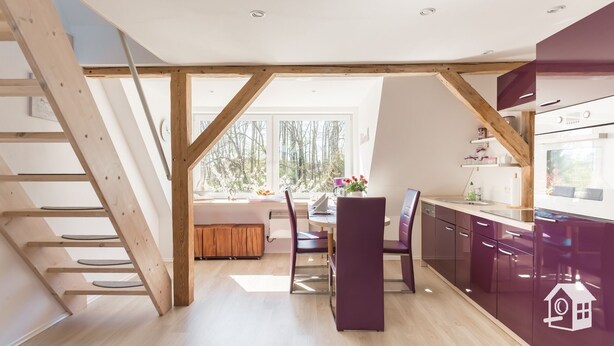 Une cuisine moderne avec des poutres en bois, un coin repas avec une table et des chaises, et une vue sur les arbres à travers de grandes fenêtres.