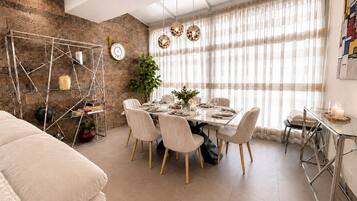 A dining area with a table set for four, surrounded by chairs, a potted plant, and a decorative wall with a clock.