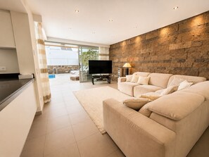 A modern living room with a stone accent wall, a flat-screen TV, a sofa, and a view of an outdoor pool. - 5BR Villa in Costa Adeje with Private Pool (Costa Adeje)