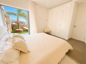 A bedroom with a large bed, a view of the outdoors, a wardrobe, and a chair.