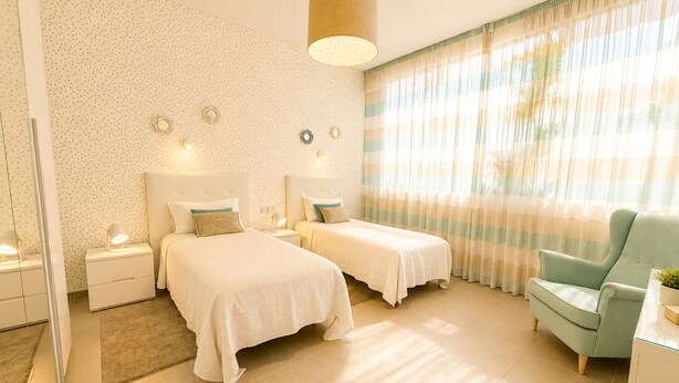Une chambre d’hôtel avec deux lits, un canapé, un miroir, une lampe et une fenêtre avec des rideaux.