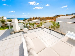 A rooftop terrace with a glass balustrade, outdoor seating, and a view of the sea and buildings. - 5BR Villa in Costa Adeje with Private Pool (Costa Adeje)