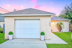 A single-story house with a white garage door, two potted plants, and a well-maintained lawn.