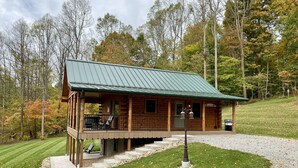 A log cabin with a porch, a covered deck, and a gravel driveway.