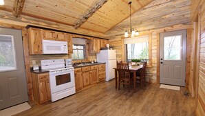 A wooden cabin-style kitchen with a dining area, featuring a stove, microwave, refrigerator, and wooden cabinets.