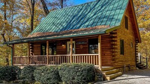 A log cabin with a green metal roof, a porch, and a gravel driveway. - Cozy Pine at Tranquil Acres (Millersburg)