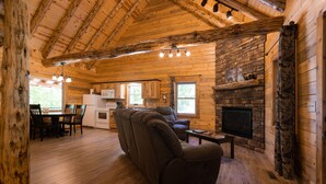 Ein Holzblockhaus-Interieur mit Kamin, Holzwänden, einer Couch, einem Essbereich und einer Küche.