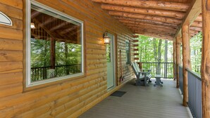 Eine Holzhütte mit überdachter Veranda, großen Fenstern und Blick auf den Wald.