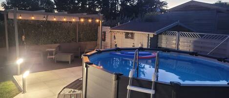 Ein Pool im Freien mit einer Leiter, umgeben von einer Terrassenfläche mit einer Pergola und Lichterketten.