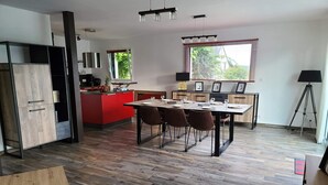 A modern kitchen with a red island, a dining area with a wooden table and chairs, and a large window with blinds. - Family house, walking distance to the beach, near St Malo (Saint-Coulomb)