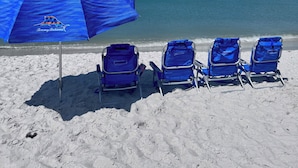 Une plage avec un parasol bleu sur lequel on peut lire « Tommy’s Bahamas » et trois chaises de plage bleues.