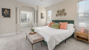 Une chambre avec un grand lit, un ventilateur de plafond, un banc et une table de chevet avec une lampe.