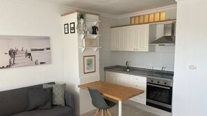 A compact living space with a kitchenette, a dining area with a table and chairs, and a sofa with cushions.