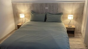 A bed with a wooden headboard, two bedside tables with lamps, and a light-colored floor.
