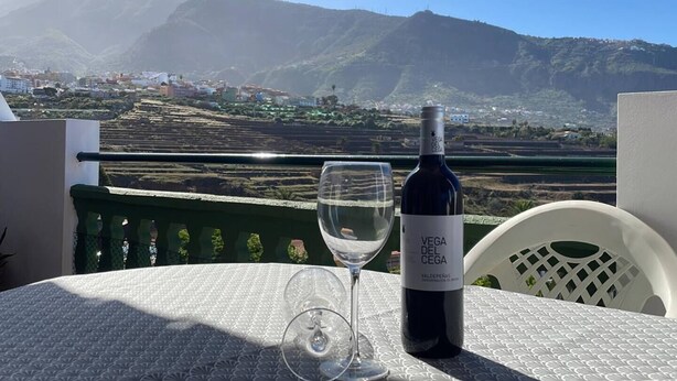 A table with a bottle of wine and a glass on a balcony overlooking a mountainous landscape.