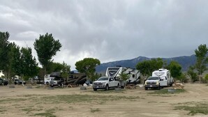 Un campament amb autocaravanes i camions estacionats sobre terra, envoltat d'arbres i muntanyes.
