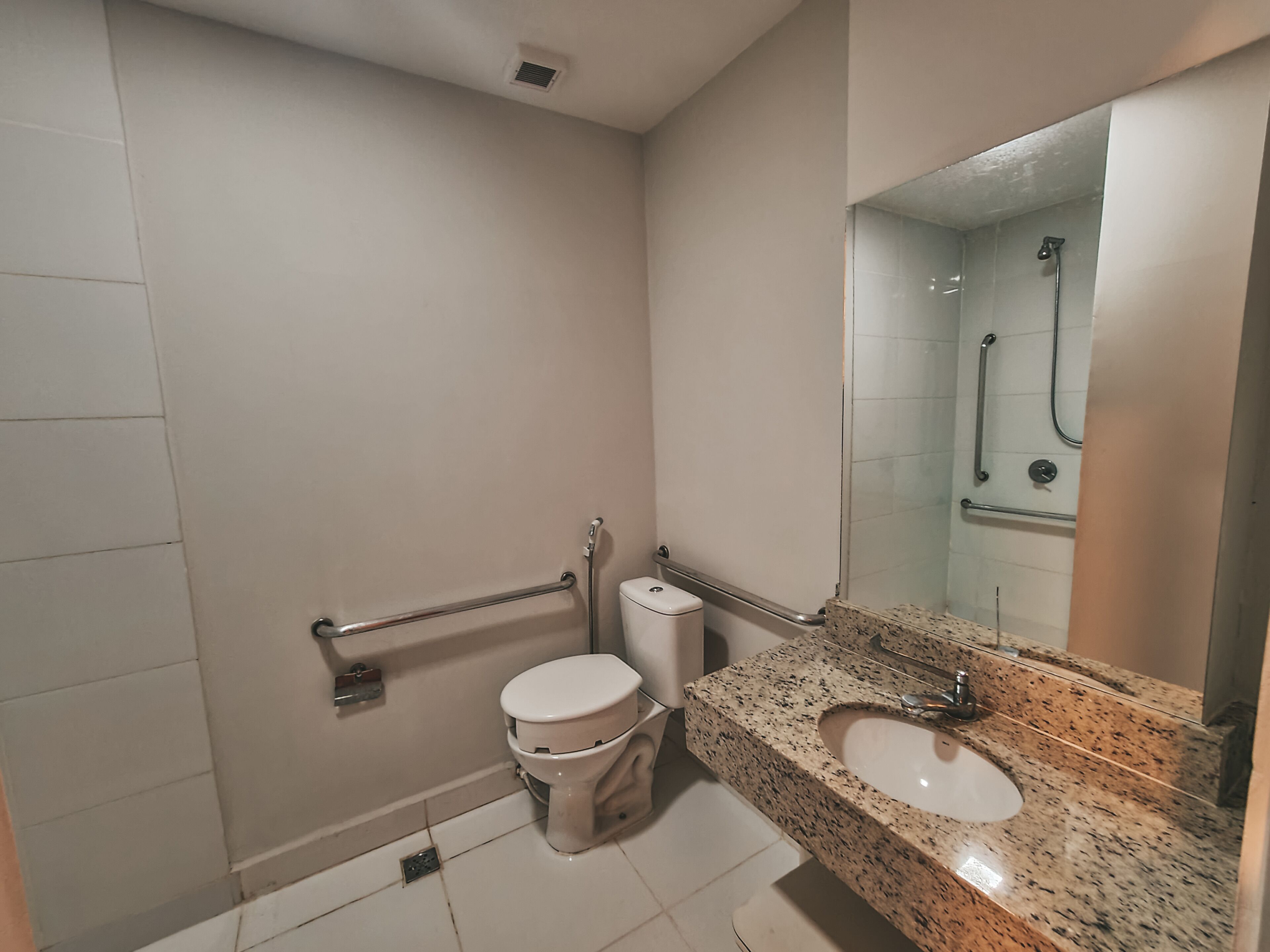 Un baño con inodoro, barras de apoyo, lavamanos y ducha.