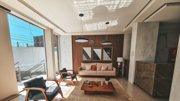 Ein modernes Wohnzimmer mit einer Couch, Sesseln, einem Couchtisch und einem großen Fenster mit Blick auf ein Gebäude.