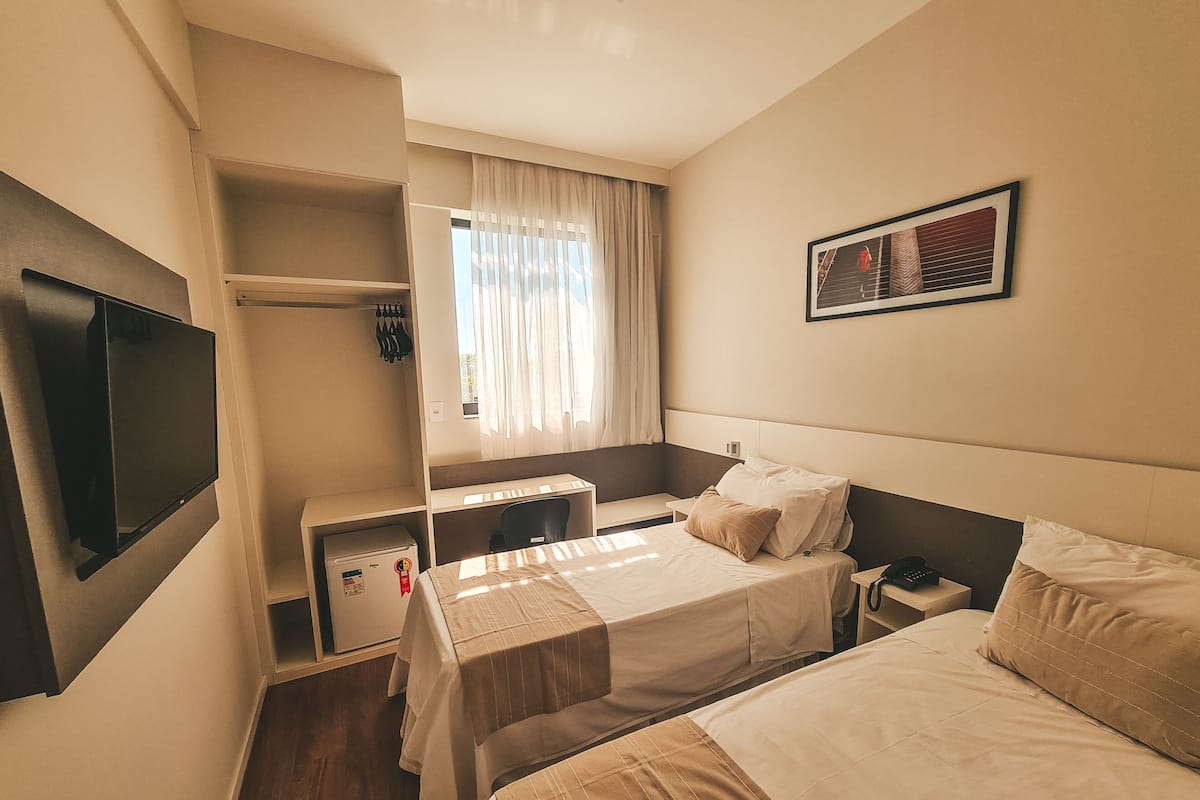 A hotel room with two beds, a desk, a TV, and a window with curtains.