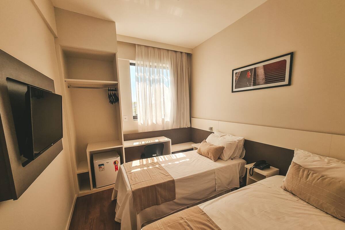 A hotel room with two beds, a desk, a TV, and a window with curtains.