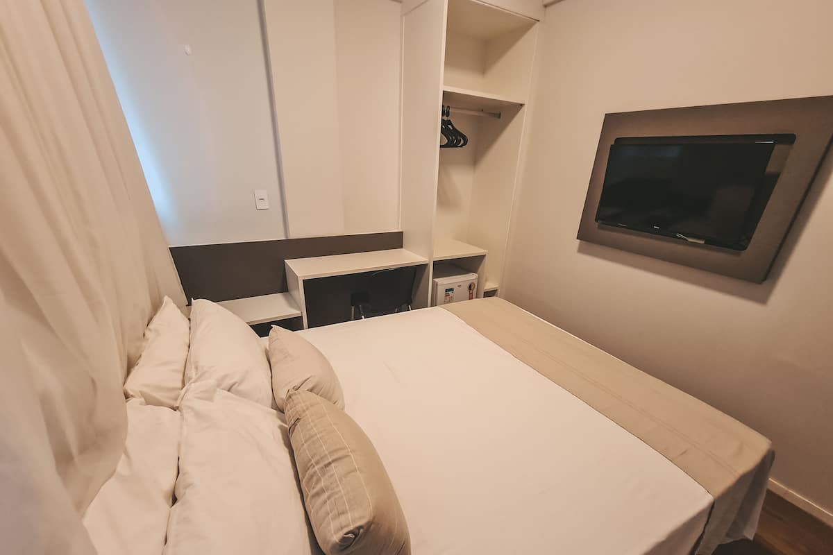 A hotel room with a bed, a desk, a chair, a TV, and a wardrobe.