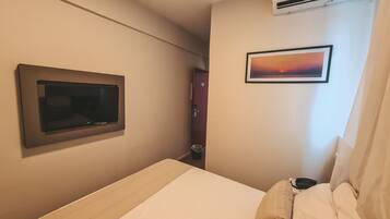 Quarto de hotel com uma cama, uma televisão montada, aparelho de ar condicionado e um quadro na parede.
