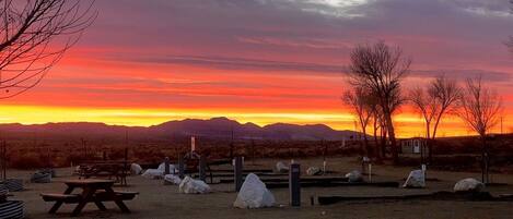 En campingplads med picnicborde, sten og en lille hytte i et ørkenlandskab ved solnedgang.