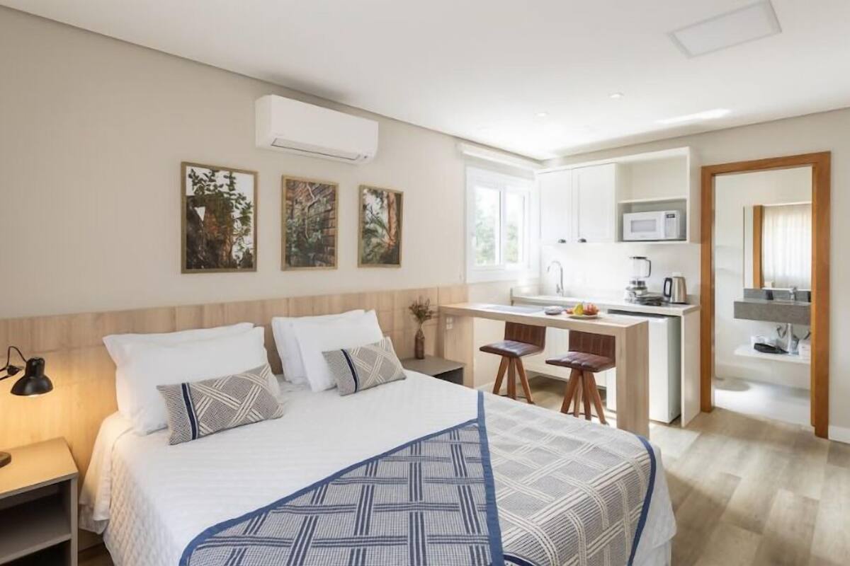 A modern bedroom with a large bed, a small desk, and a kitchenette.