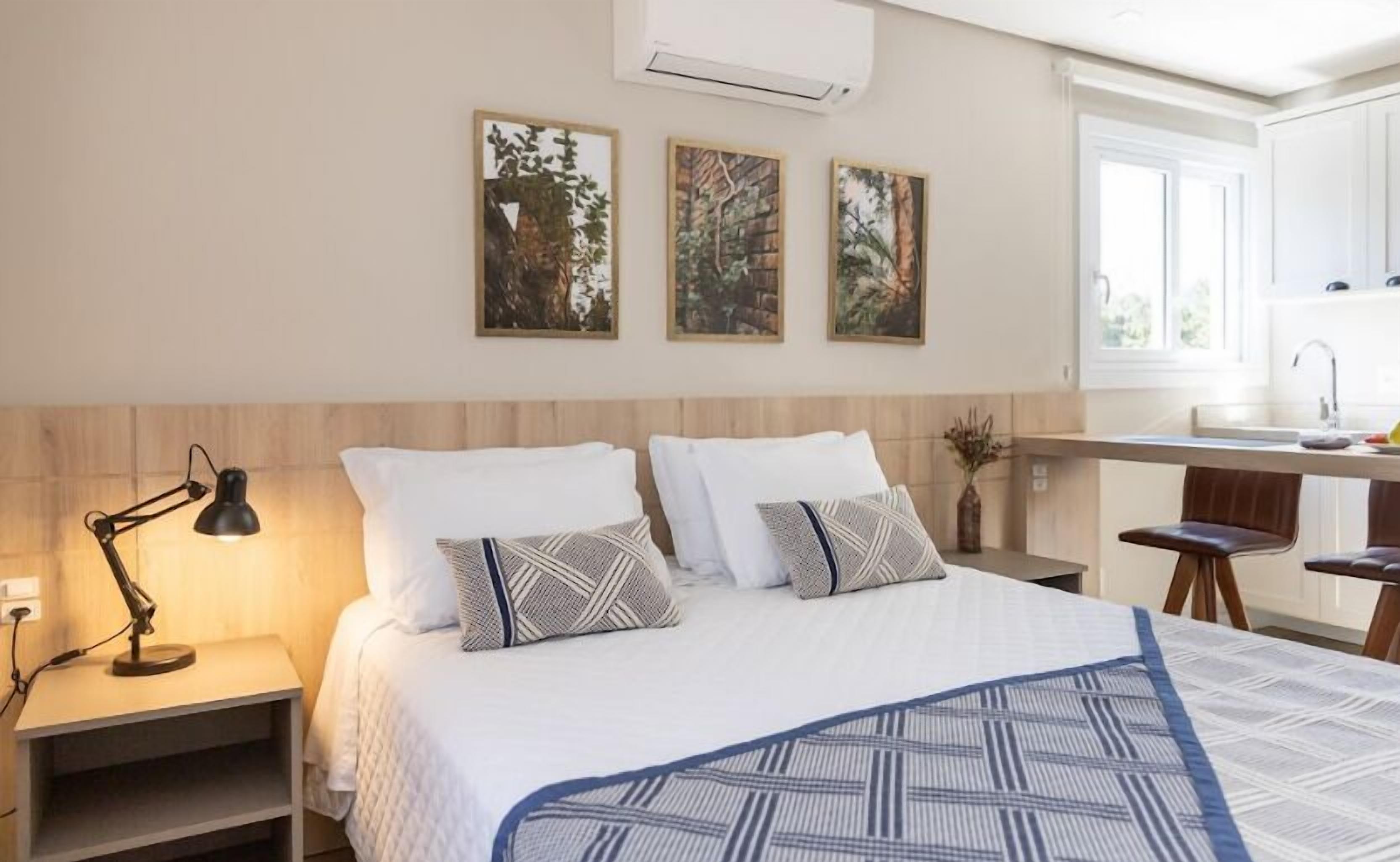 A bedroom with a bed, bedside tables, a desk, and a kitchen area.