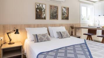 A bedroom with a bed, bedside tables, a desk, and a kitchen area.