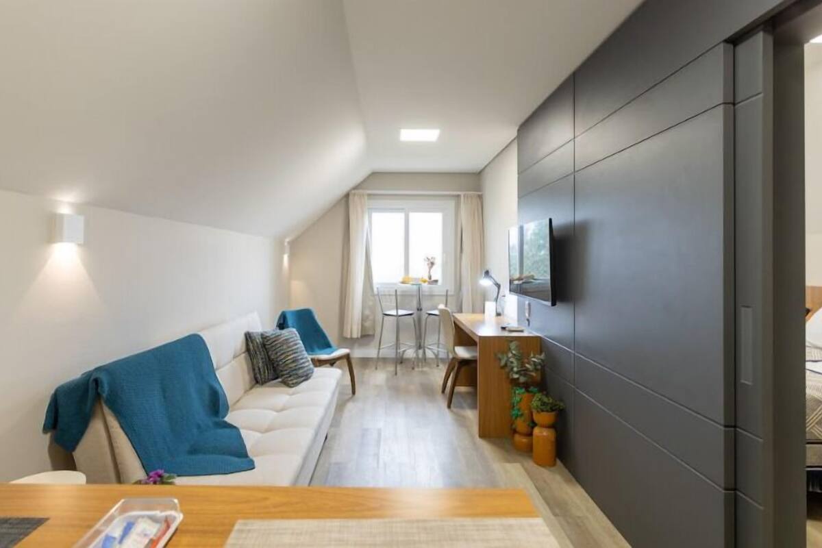A modern living room with a sofa, a dining table, and a TV mounted on the wall.