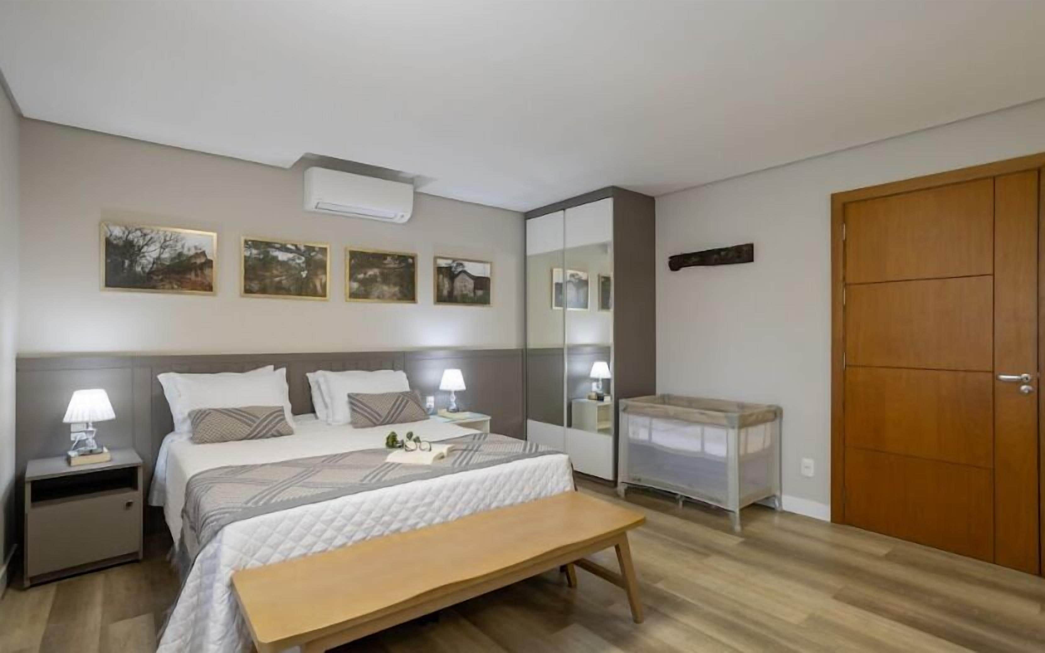 A bedroom with a bed, bedside tables with lamps, a bench, a wardrobe, and wall-mounted artwork.