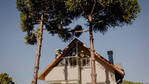 A two-story house with a gabled roof, large windows, and a visible chimney. - VILLARY FLATS (Gramado)