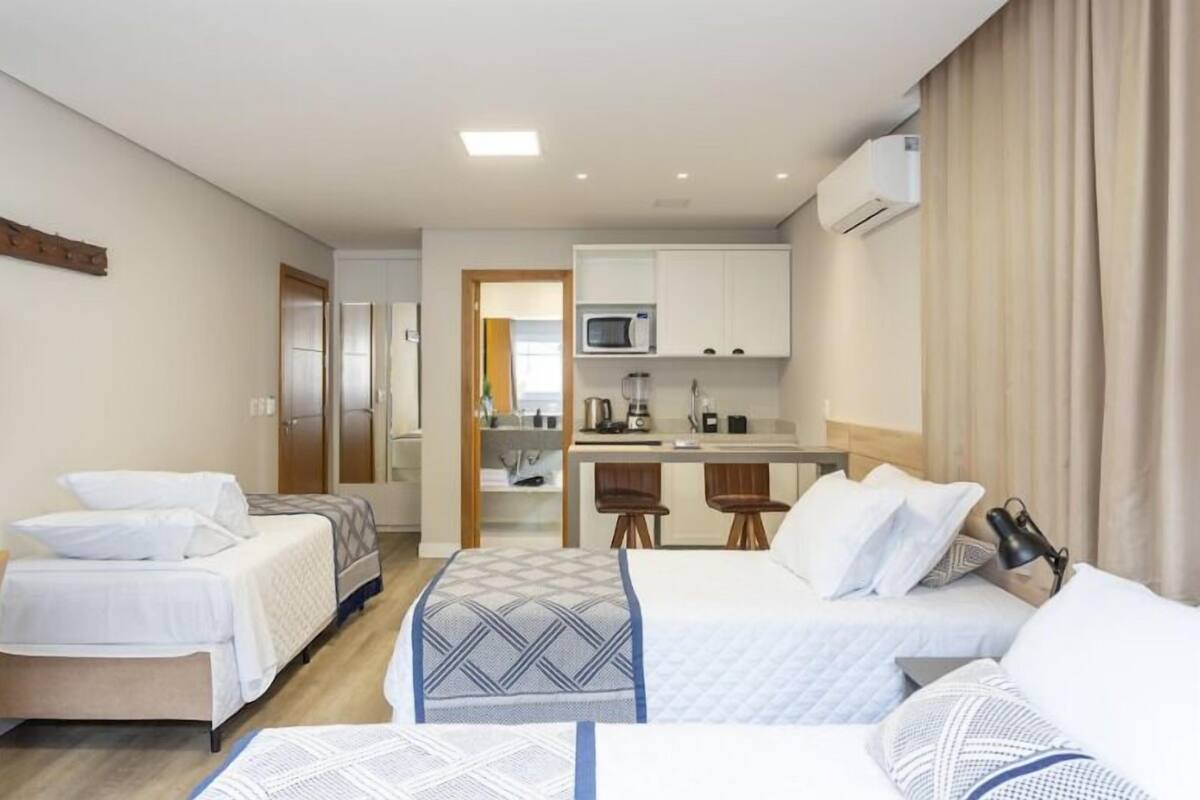 A hotel room with two beds, a kitchenette, and a bathroom.