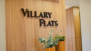 A wooden reception desk with the name "VILLARY FLATS" and two potted plants. - VILLARY FLATS (Gramado)