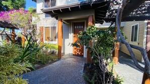 A two-story house with a covered porch, a front door, and a small garden area with various plants and a tree. - Golf Villas at Mauna Lani Q22 -1,460 sq Beach Club Access (Waimea)