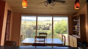 A dining area with a table and chairs, a ceiling fan, and a view of a forest through large windows. - Panoramic views on 50 private acres! (Escalante)