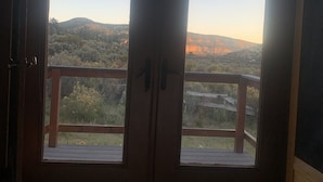 A room with a bed and a view through a door to a balcony with a railing. - Panoramic views on 50 private acres! (Escalante)