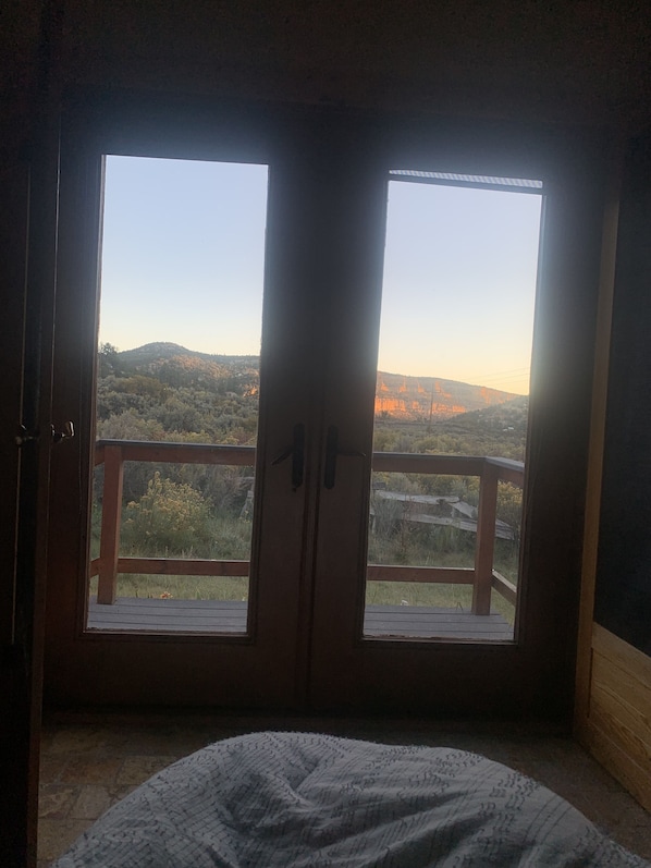 A room with a bed and a view through a door to a balcony with a railing. - Panoramic views on 50 private acres! (Escalante)
