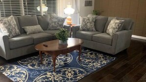 Ein Wohnzimmer mit zwei grauen Sofas, einem Holztisch und einem gemusterten Teppich.
