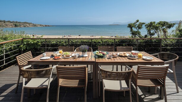 A wooden deck with a table set for dining, overlooking a beach and the sea.