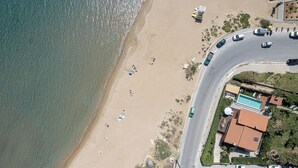 An aerial view of a beach with a road curving around it, a swimming pool, and several parked cars.